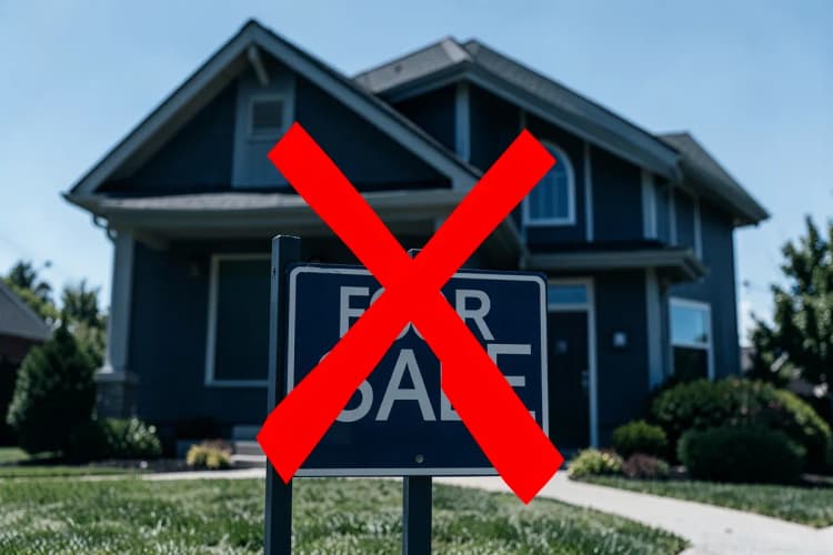 Uma casa com uma placa de "Vende-se" e um X vermelho sobre ela.