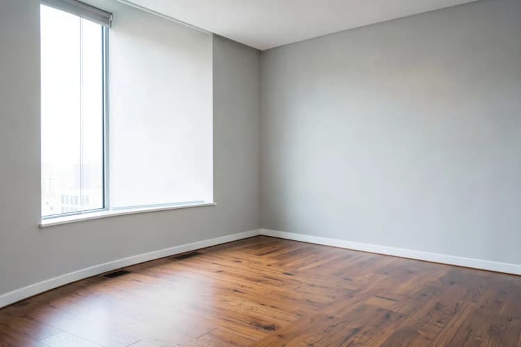 Uma sala comercial vazia com piso de madeira e paredes claras, vista de um canto.