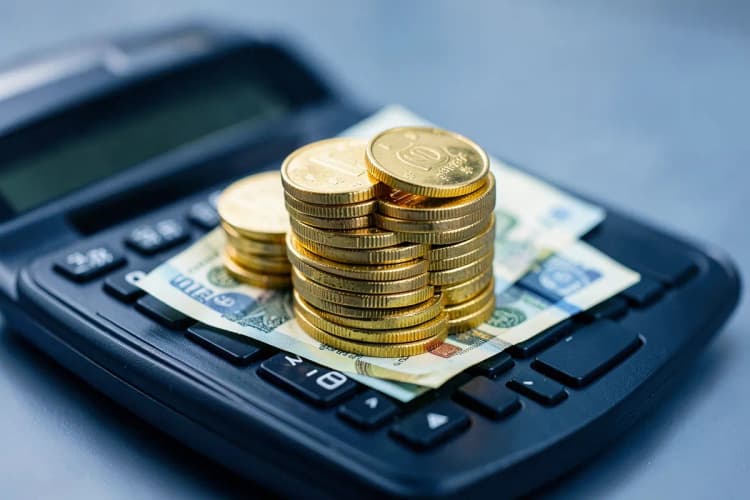Uma pilha de moedas de ouro e notas de dinheiro em cima de uma calculadora, simbolizando o custo do usucapião.