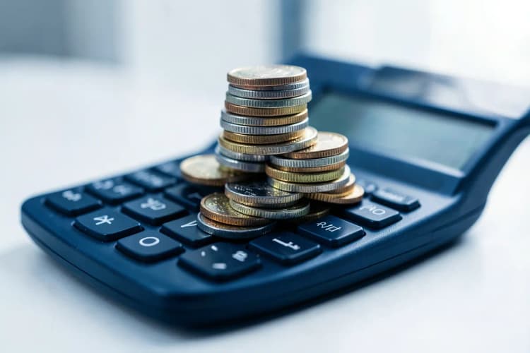 Moedas de diferentes valores empilhadas sobre uma calculadora.