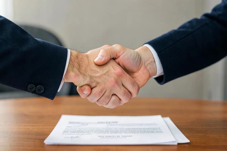 Duas pessoas apertando as mãos sobre um contrato de locação, simbolizando acordo.