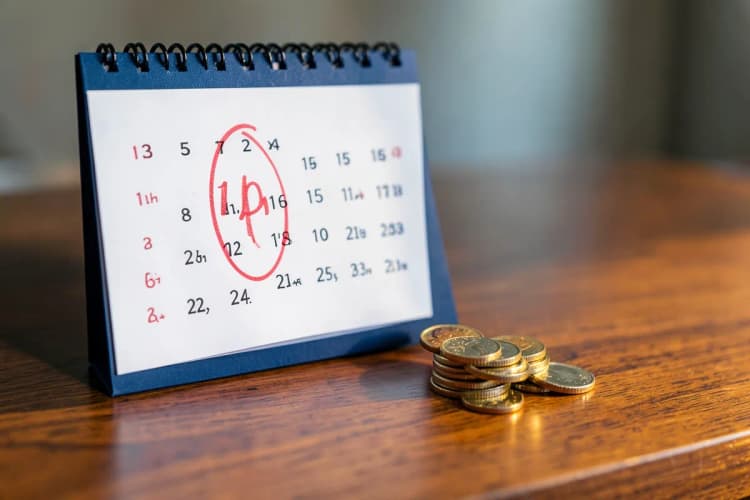Um calendário com o dia 10 marcado em vermelho, ao lado de uma pequena pilha de moedas.