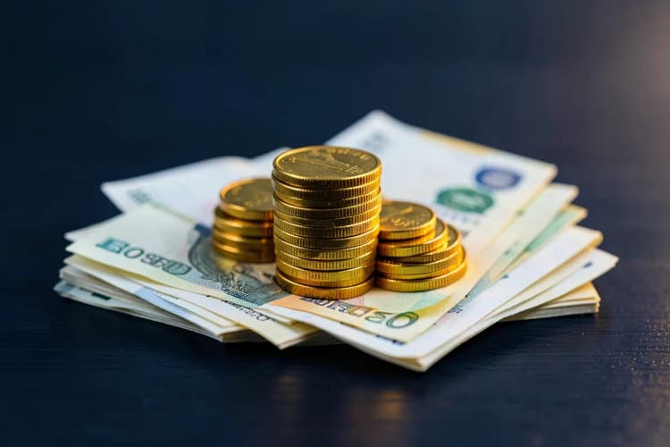 Uma pilha de moedas de ouro e notas de dinheiro dobradas sobre uma superfície de madeira escura.