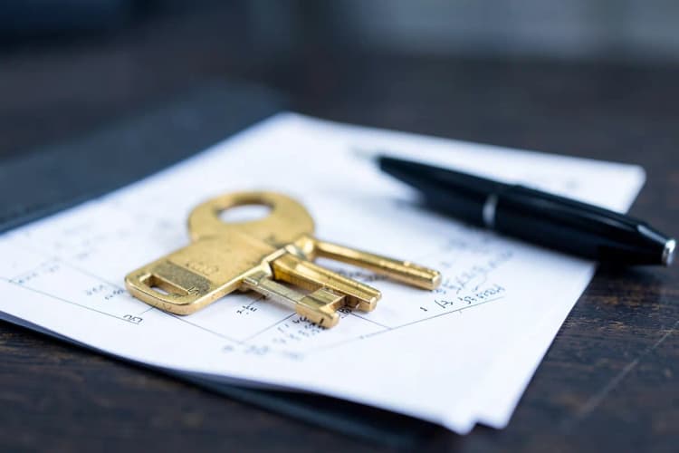 Chave de casa sobre um contrato imobiliário com uma caneta ao lado.