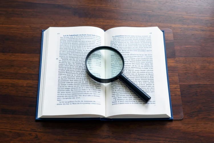Livro de leis aberto sobre uma mesa com uma lupa.