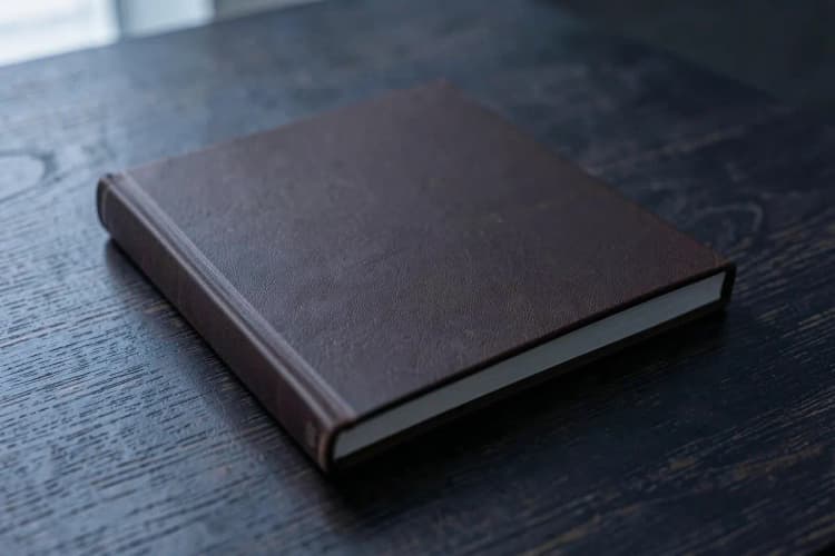 Um livro de capa dura fechado sobre uma mesa de madeira escura.